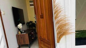 A hallway with a wooden door, a doormat with "Tintara Cozy Homes" text, a white vase with pampas grass, and a TV on the wall. - TiniTara Cozy Home (Dar es Salaam, Tanzania)
