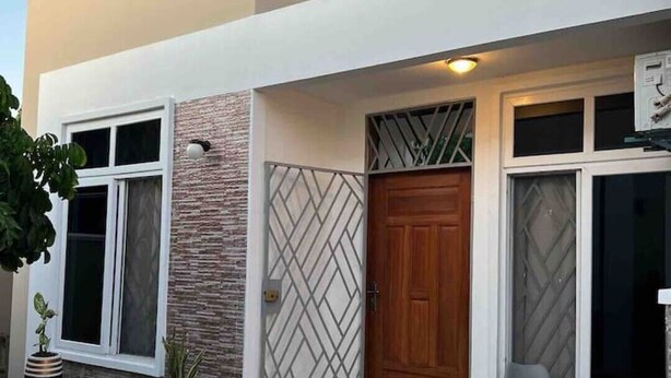 A modern building with a stone facade, a wooden door, and a tiled entrance area. - TiniTara Cozy Home (Dar es Salaam, Tanzania)