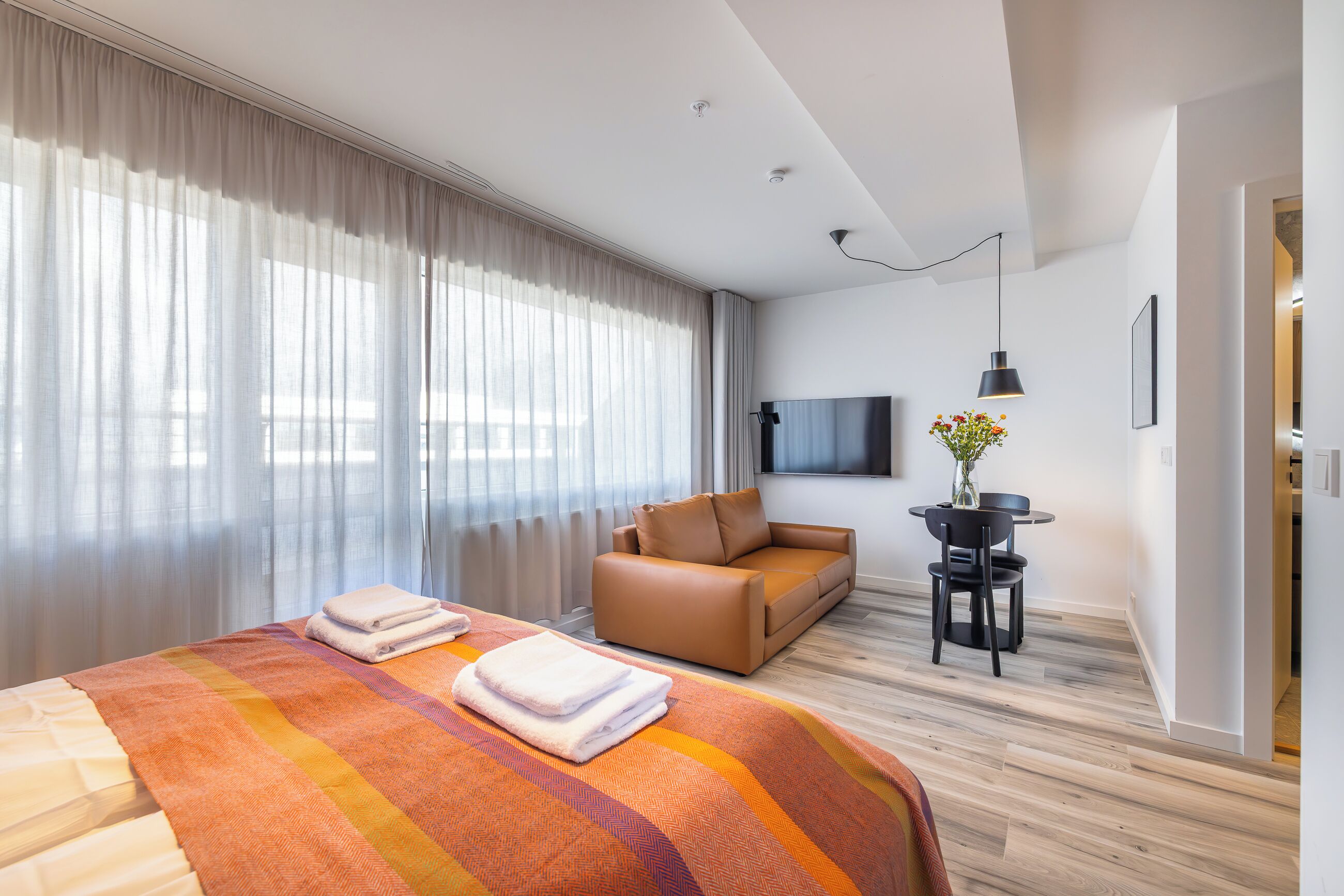 Une chambre d’hôtel moderne dotée d’un grand lit, d’un canapé, d’une télévision à écran plat et d’une petite table sur laquelle est posé un vase.