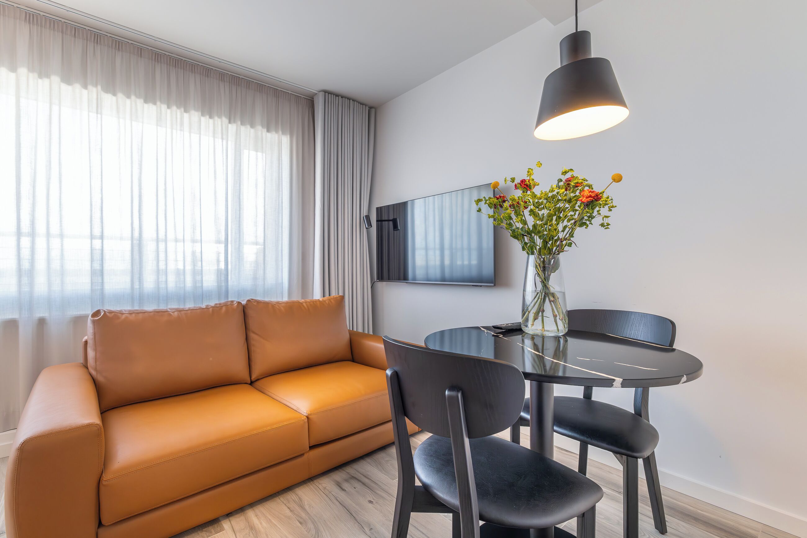 Ein modernes Wohnzimmer mit einem braunen Ledersofa, einem runden Glastisch und einer Blumenvase.