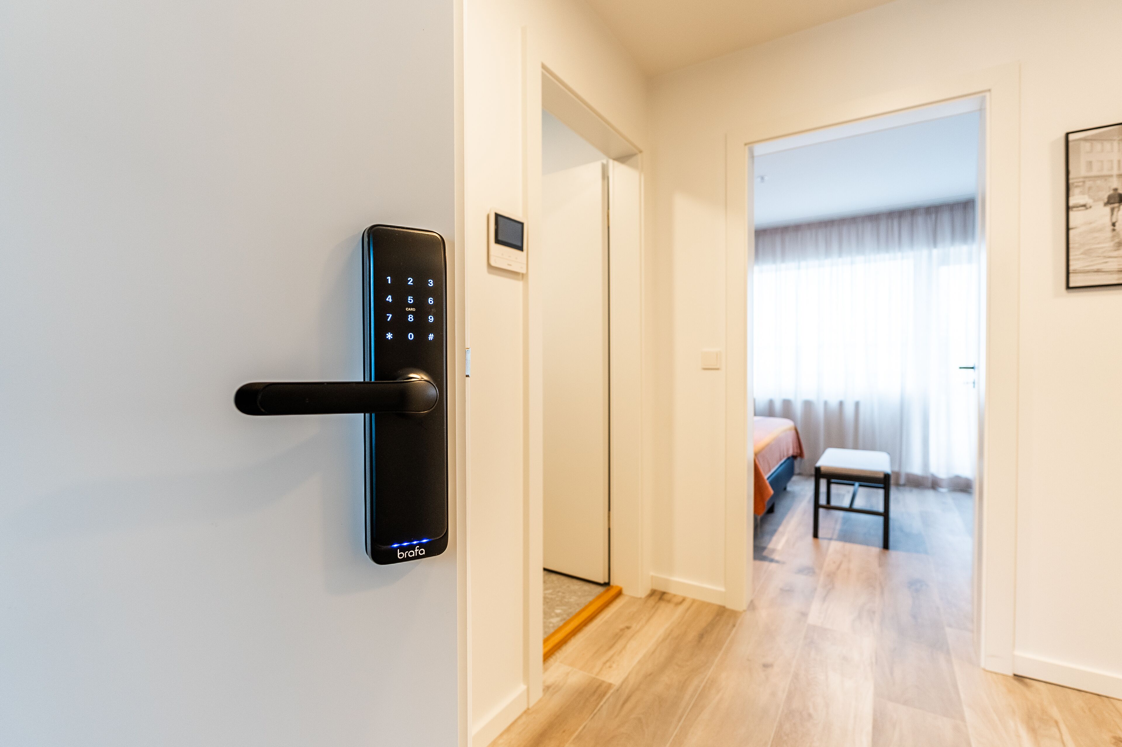 A modern room with a digital lock on the door, a small table, and a bed with a window.