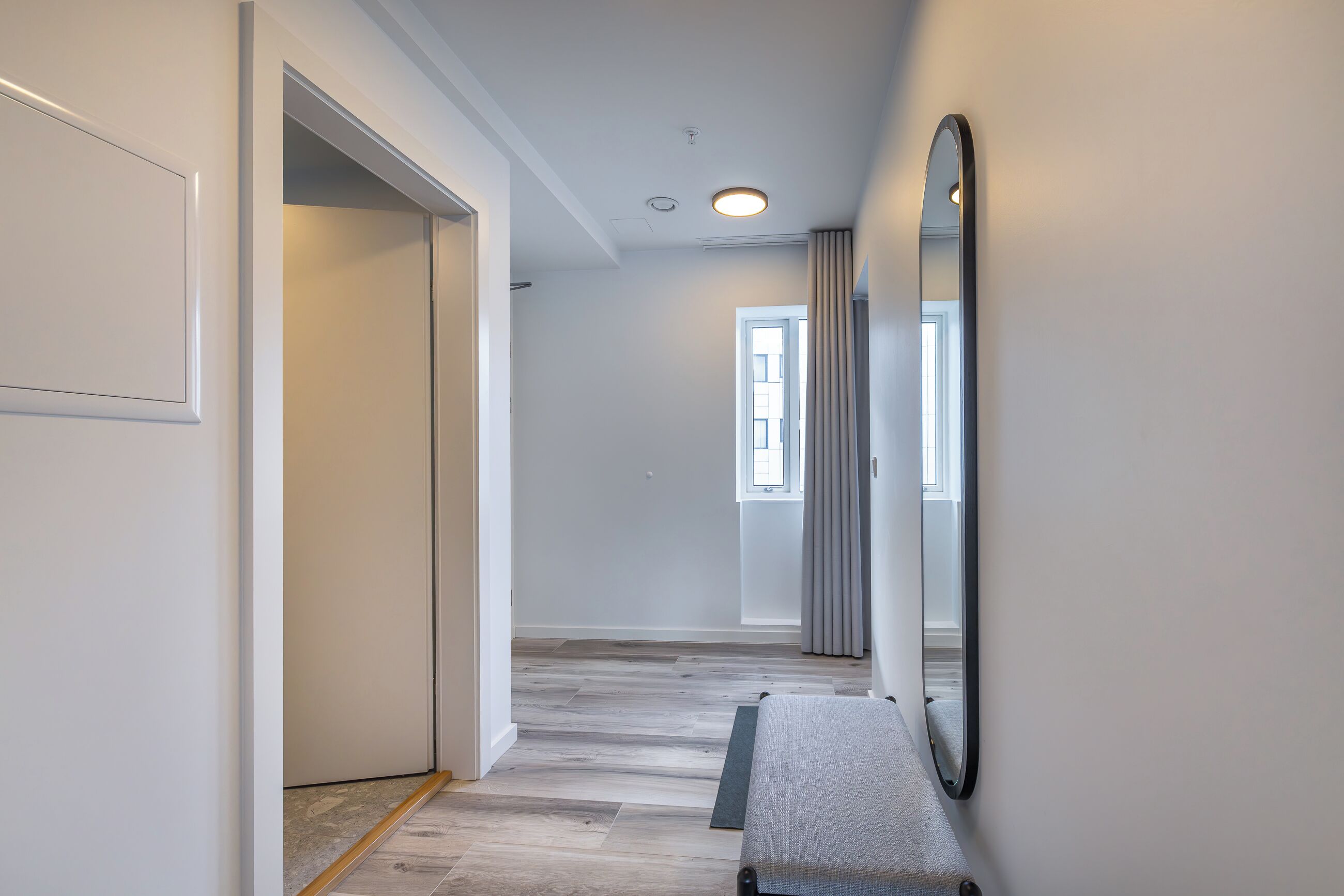 A hallway with a bench, a large mirror, and a door leading to another room.