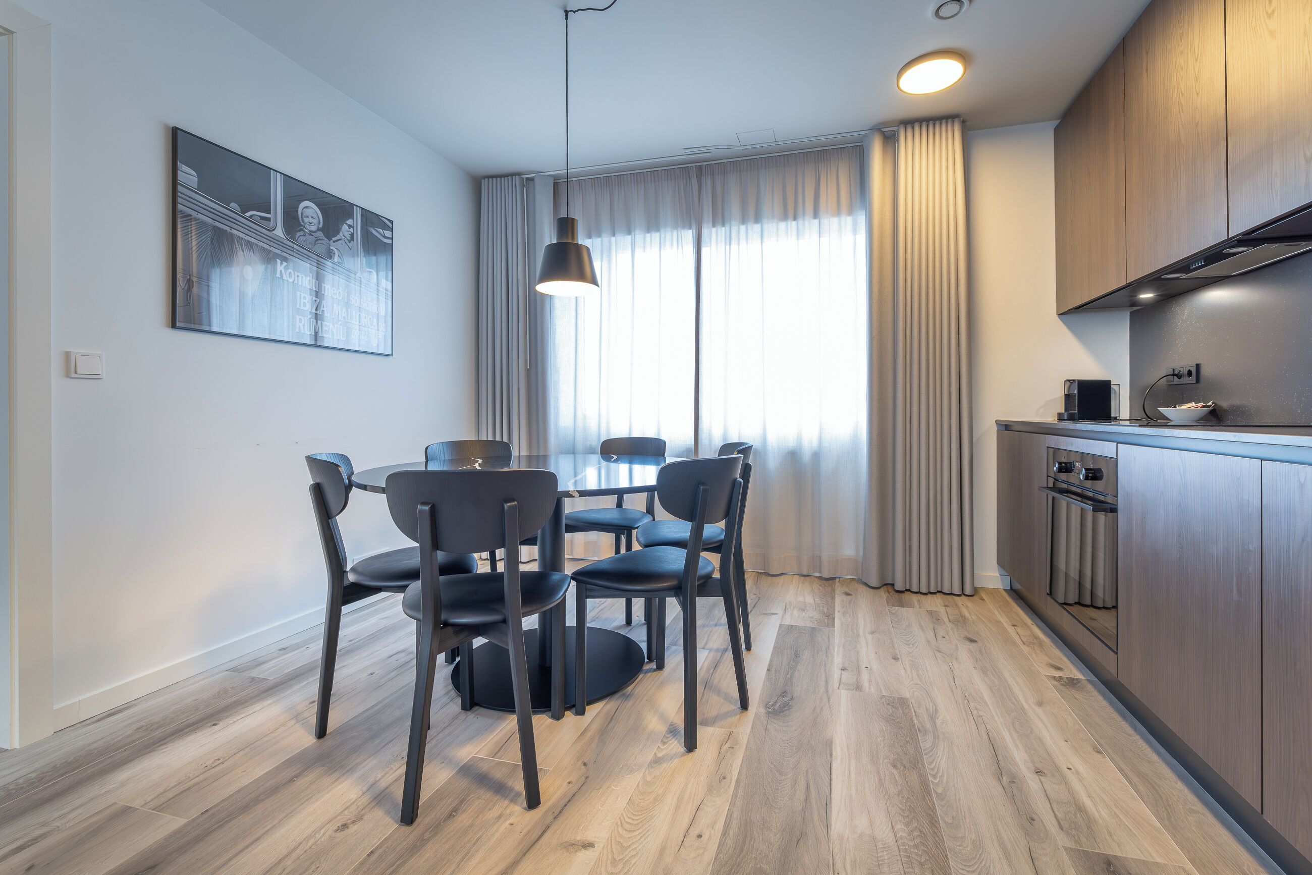 A modern kitchen with wooden cabinets, a dining area with a round table and chairs, and a pendant light.