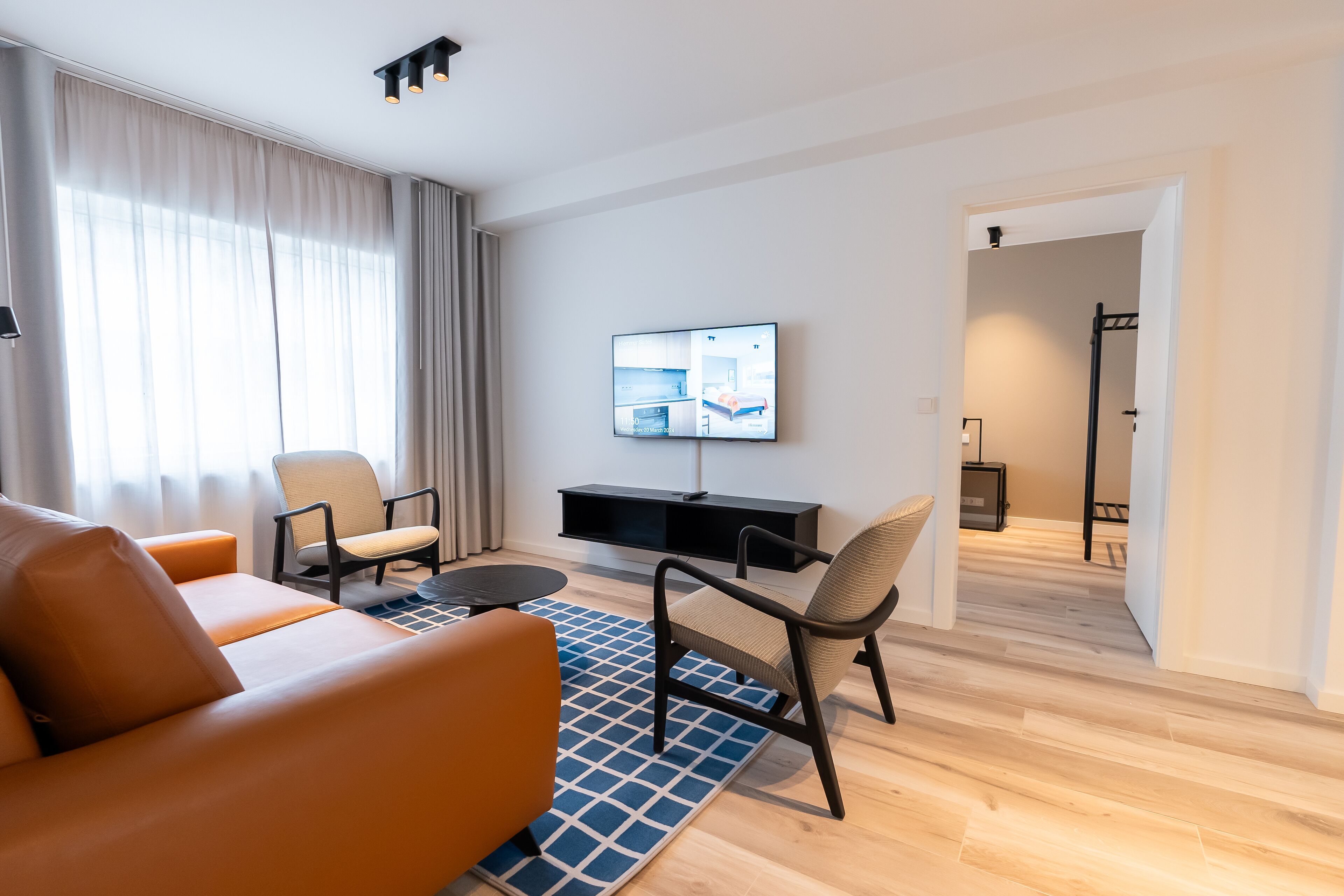 A modern living room with a sofa, chairs, a TV, and a wooden floor.