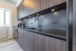A modern kitchen with a dark countertop, stainless steel sink, and wooden cabinets.