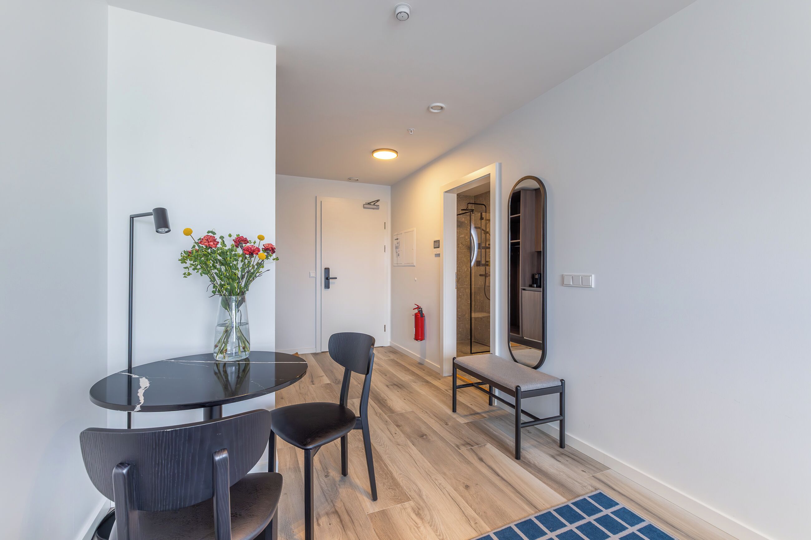 A modern room with a dining table, chairs, a vase with flowers, a bench, and a mirror.