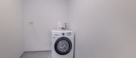 A small laundry room with a front-loading washing machine and a detergent bottle on top.