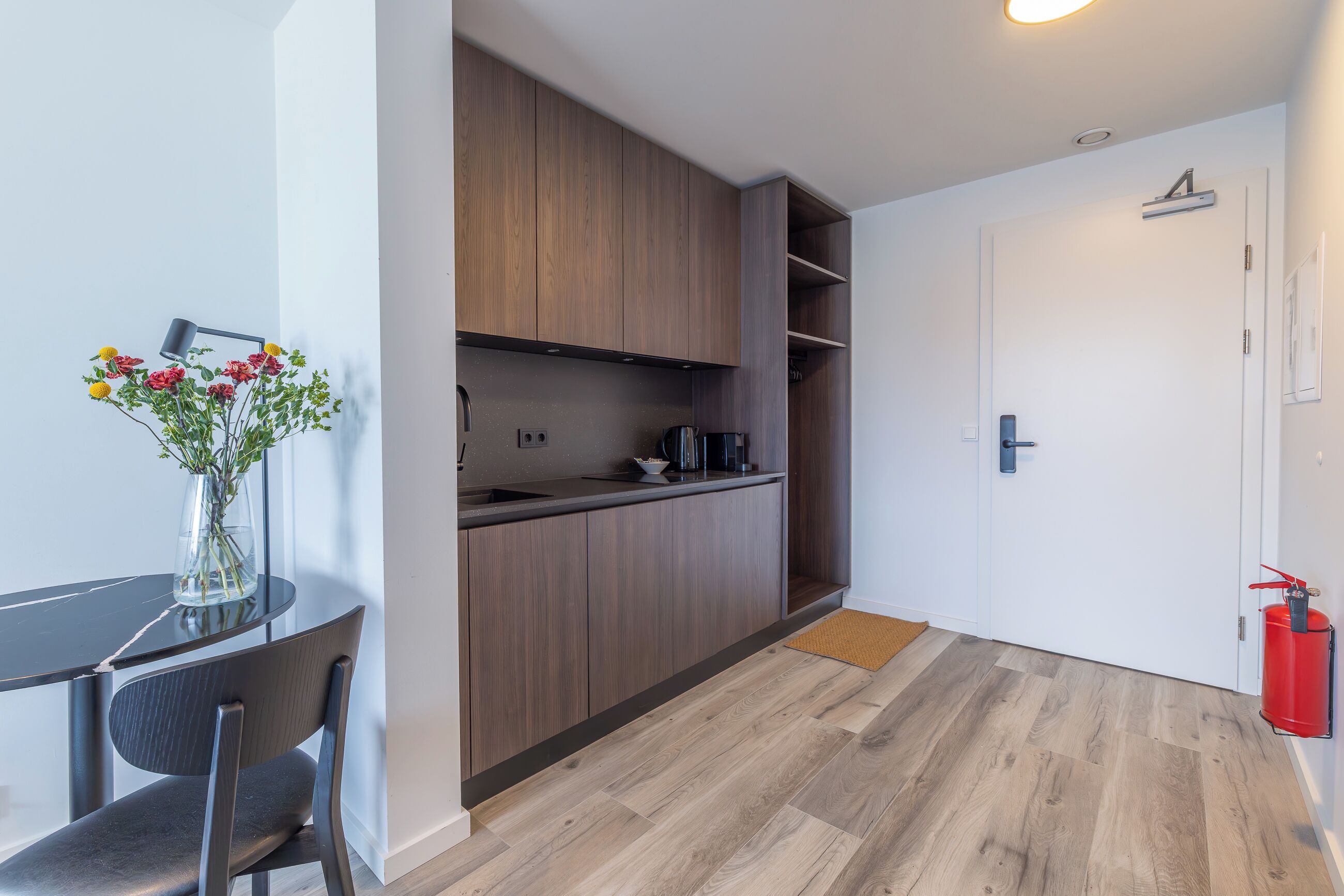 Een moderne keuken met houten kastjes, een koffieapparaat en een vaas met bloemen op het aanrecht.