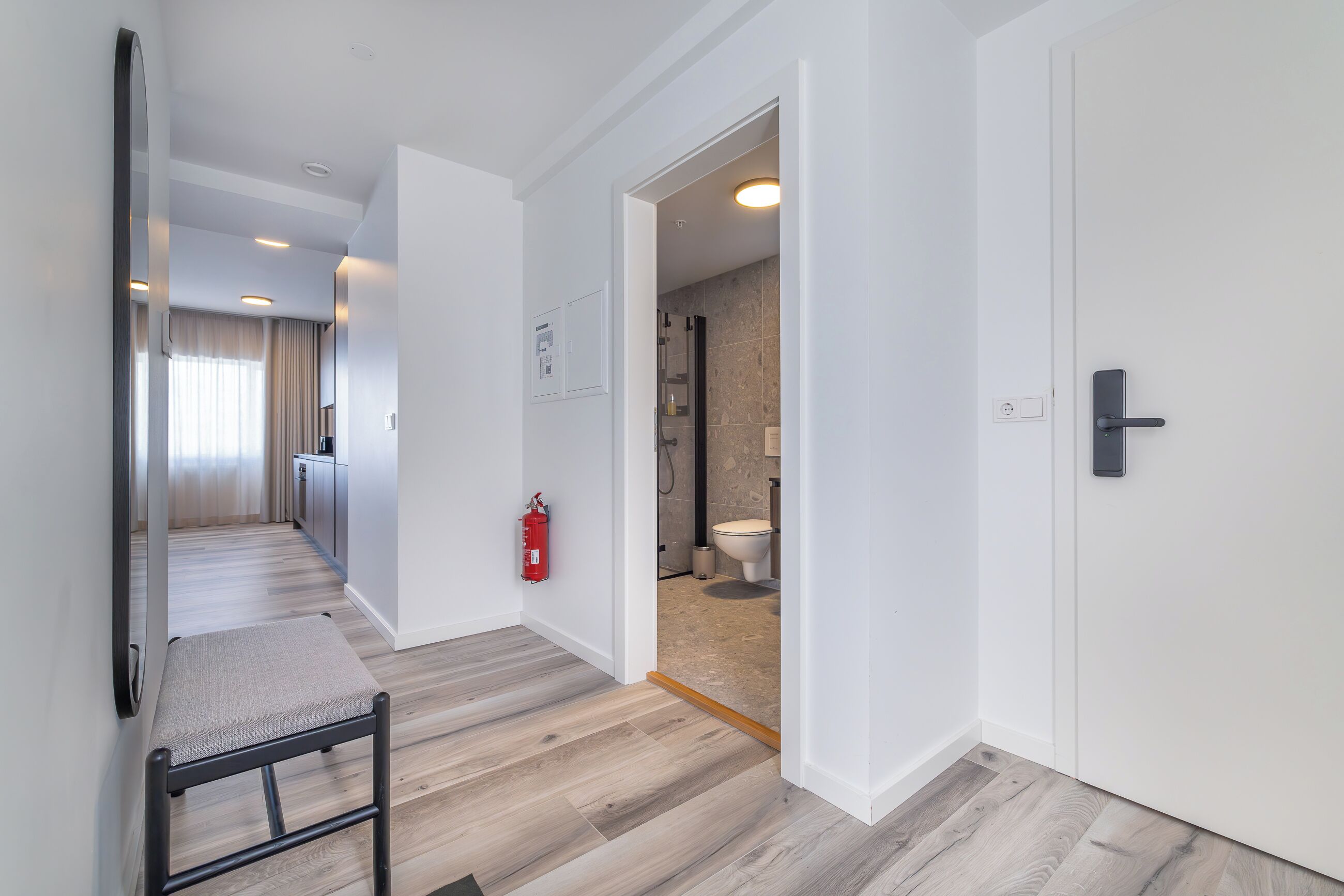A hallway with a wooden floor, a bench, and a door leading to a bathroom.