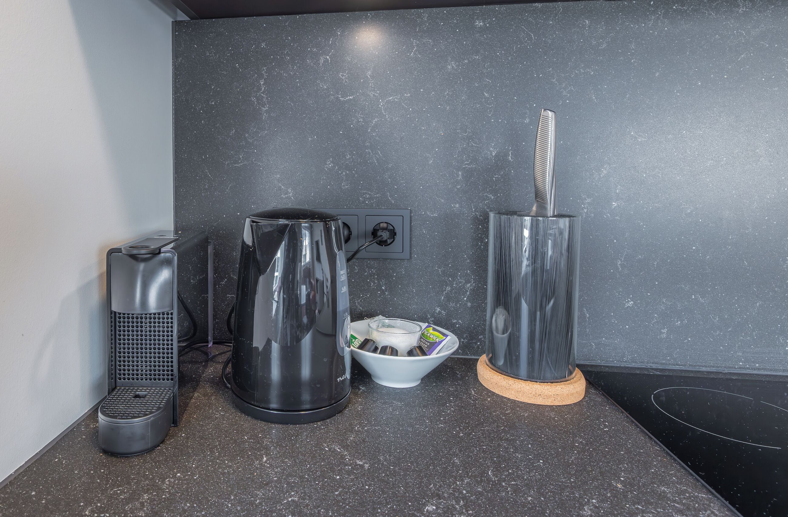 A kitchen with a coffee maker, a kettle, and a toaster on a granite countertop.