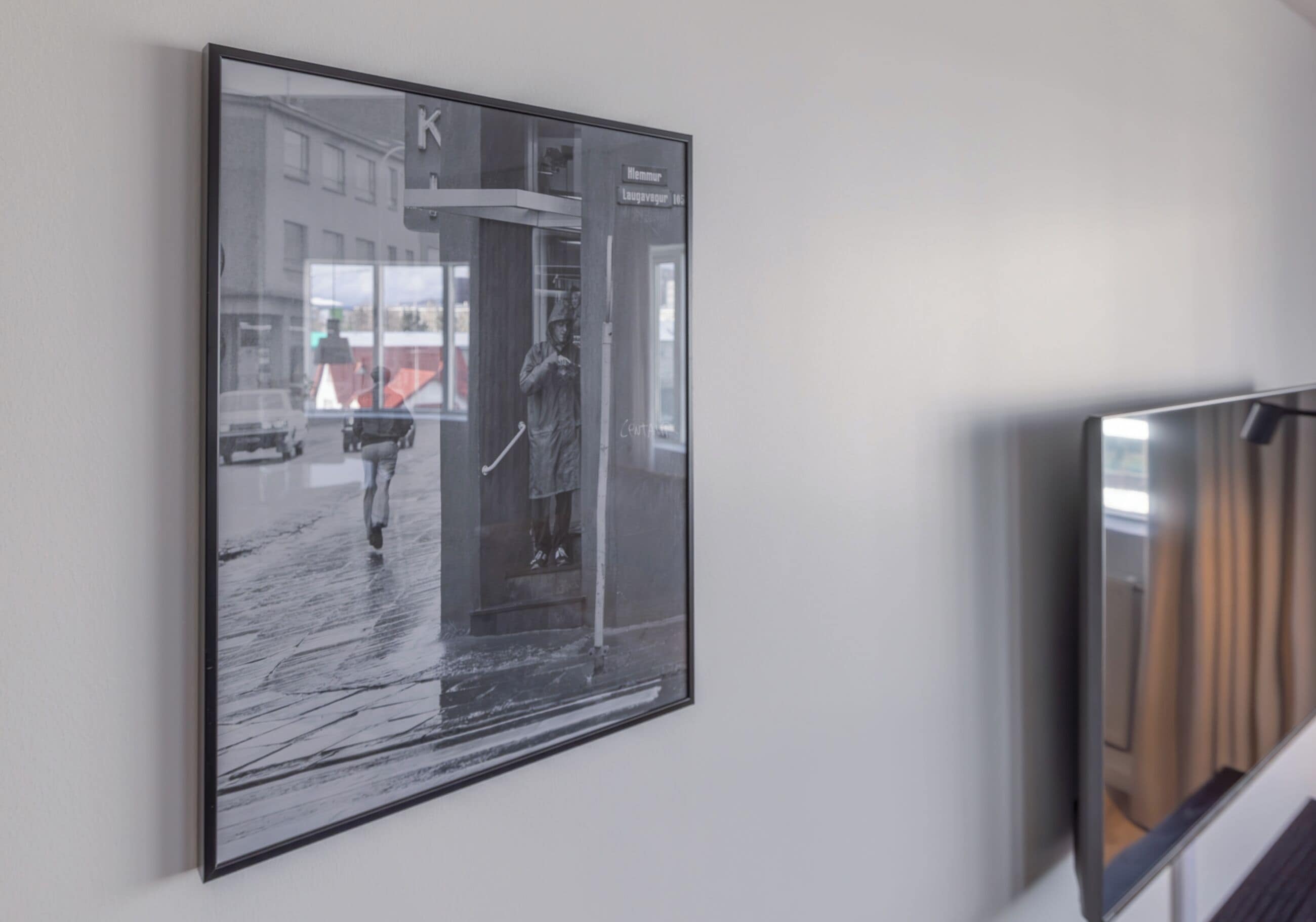 A framed photograph of a rainy street scene with a person walking, mounted on a wall.