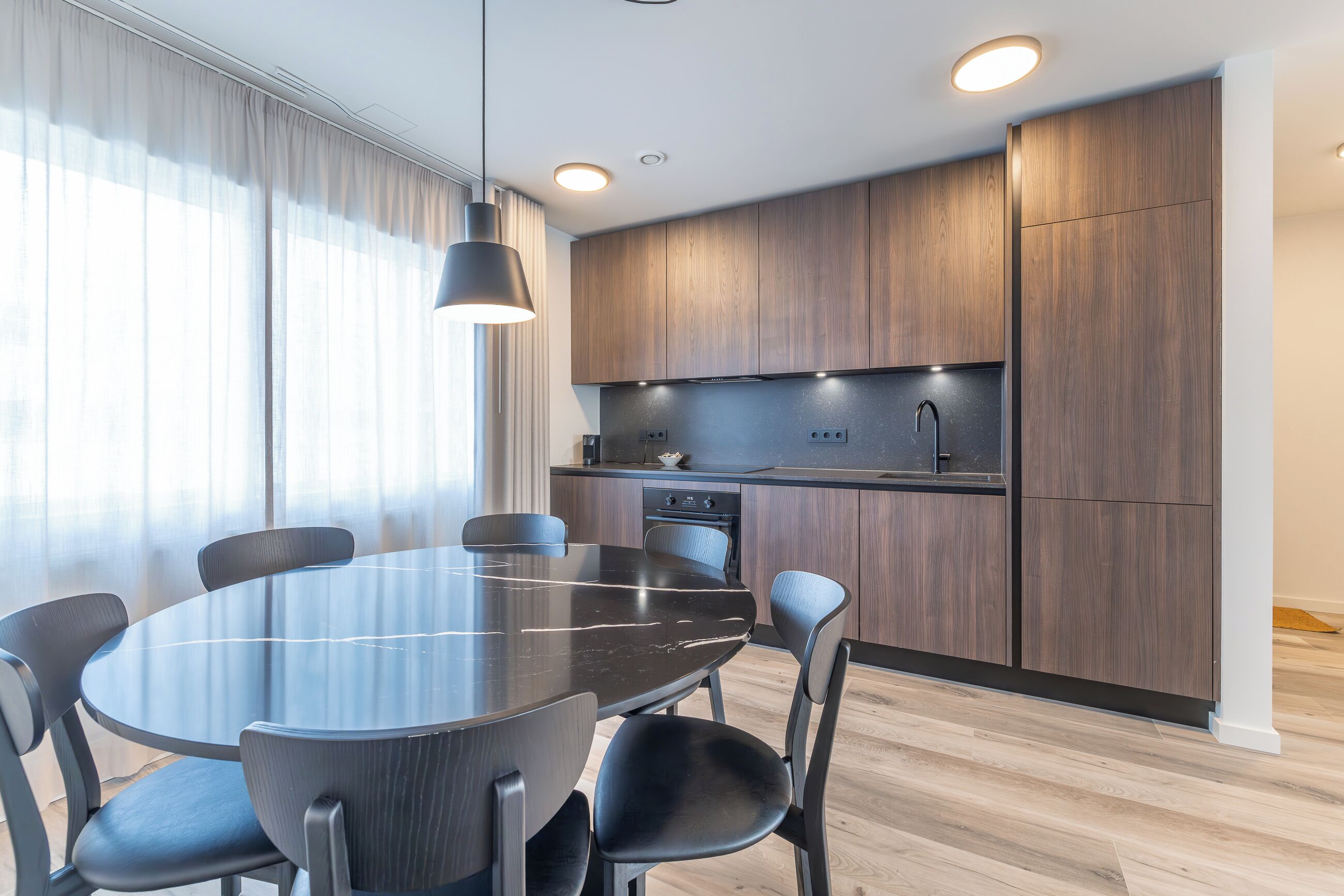 Una cocina moderna con armarios de madera oscura, una encimera negra y una mesa redonda con sillas.