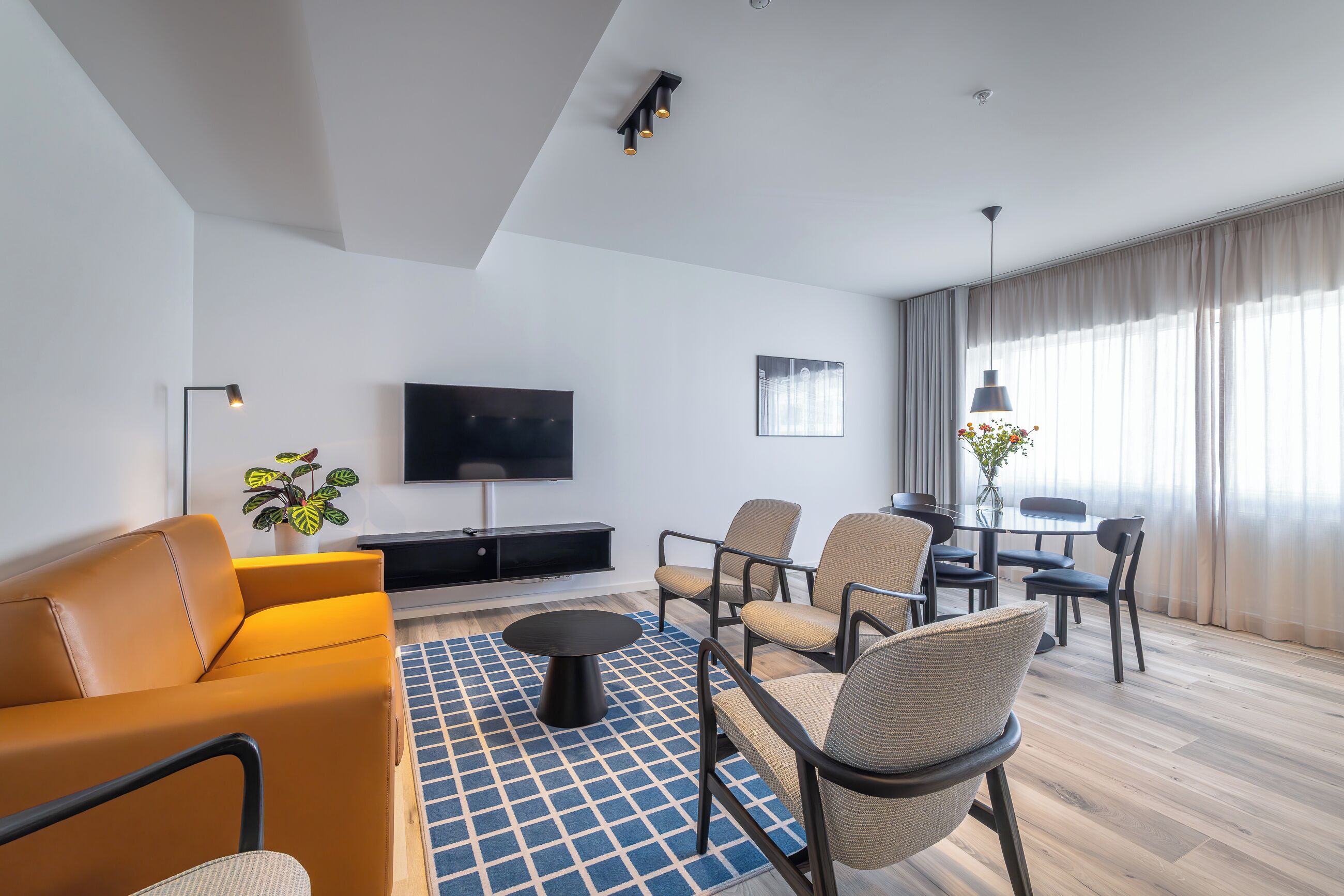 A modern living room with a sofa, chairs, a coffee table, a TV, and a dining area with a table and chairs.