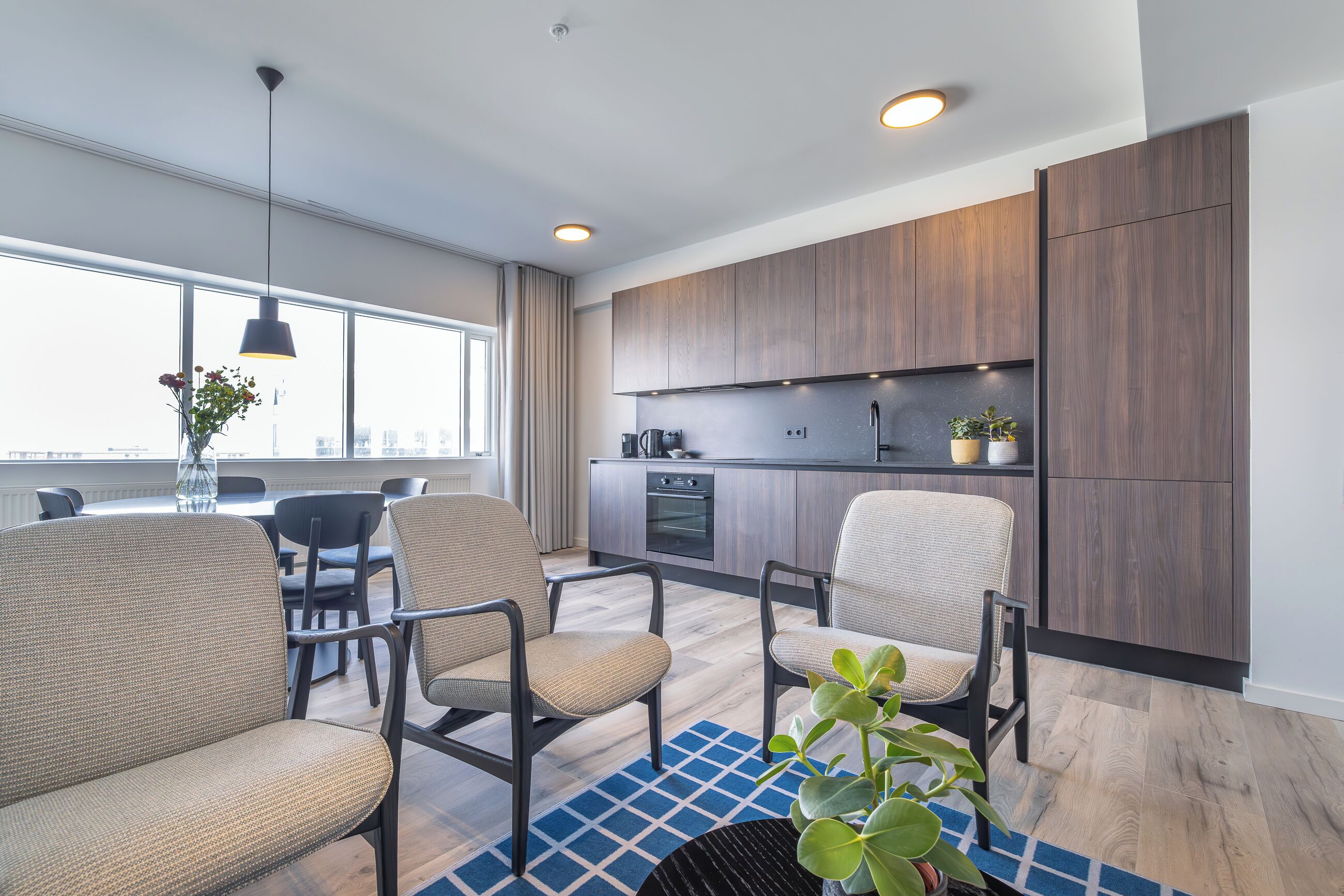 A modern kitchen with wooden cabinets, a dining area with chairs, and a large window providing natural light.