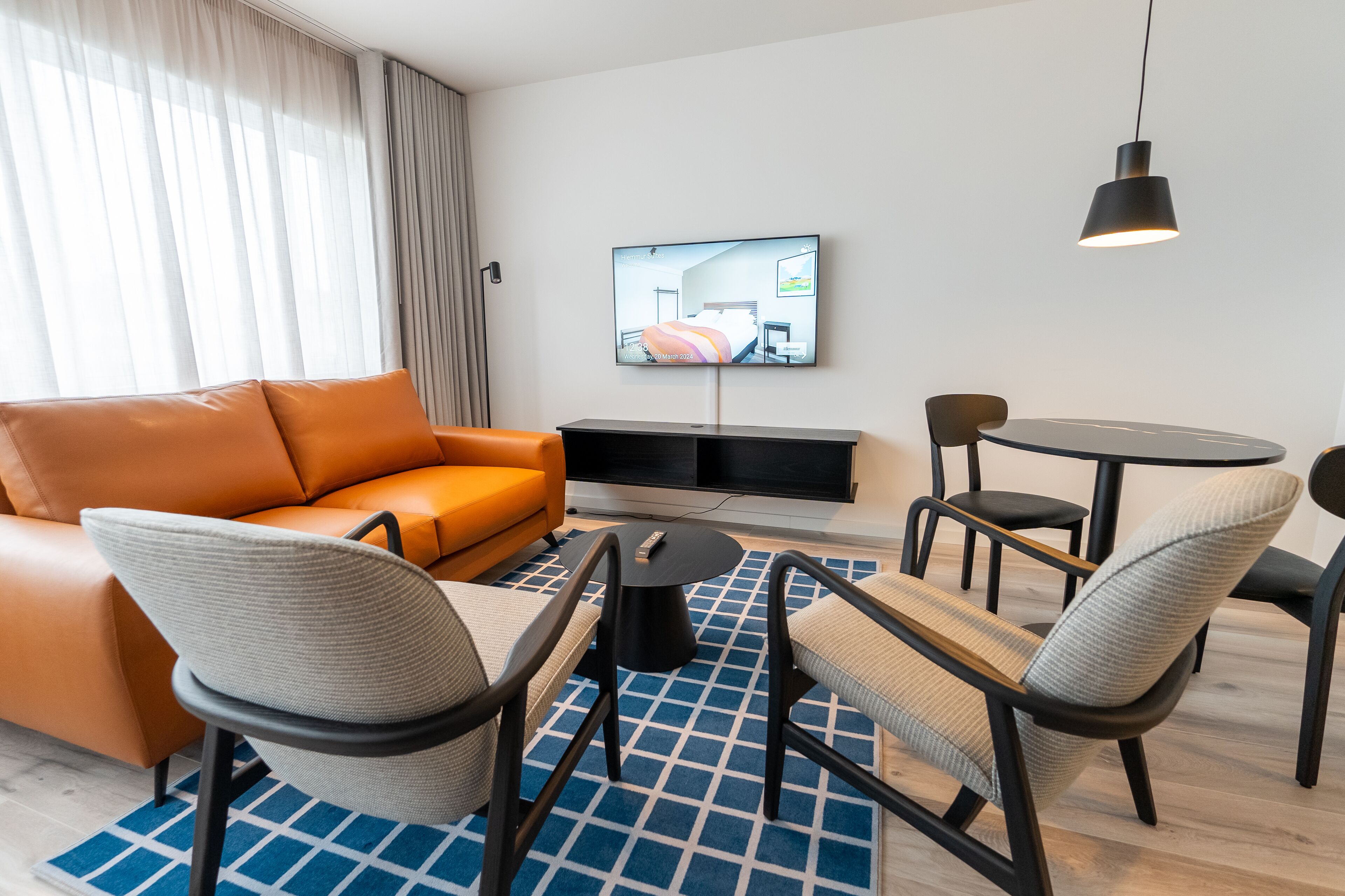A modern hotel room with a sofa, chairs, a TV, and a dining table.
