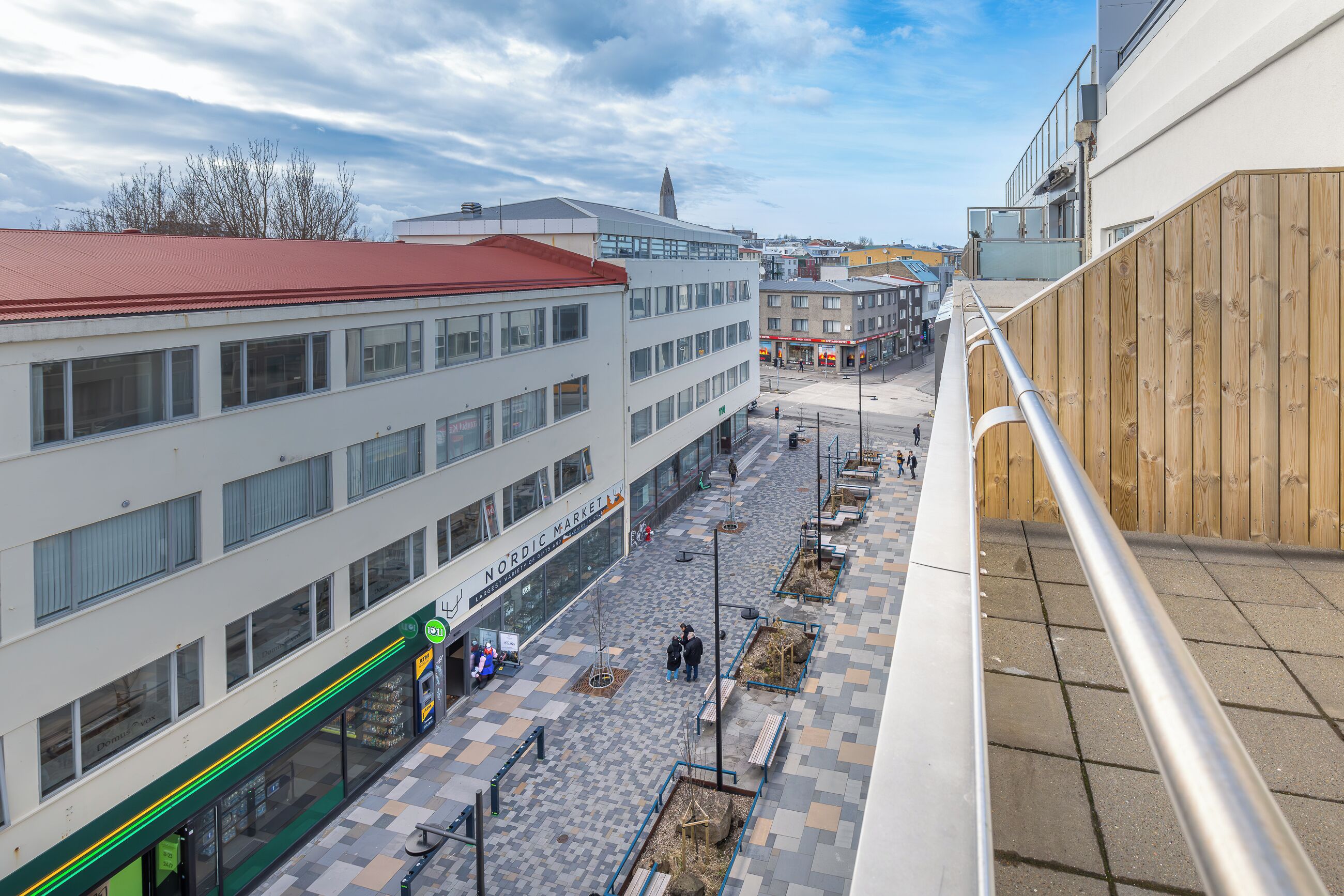 A high-rise building with a red roof, a Nordic Market, and a pedestrian walkway with benches.