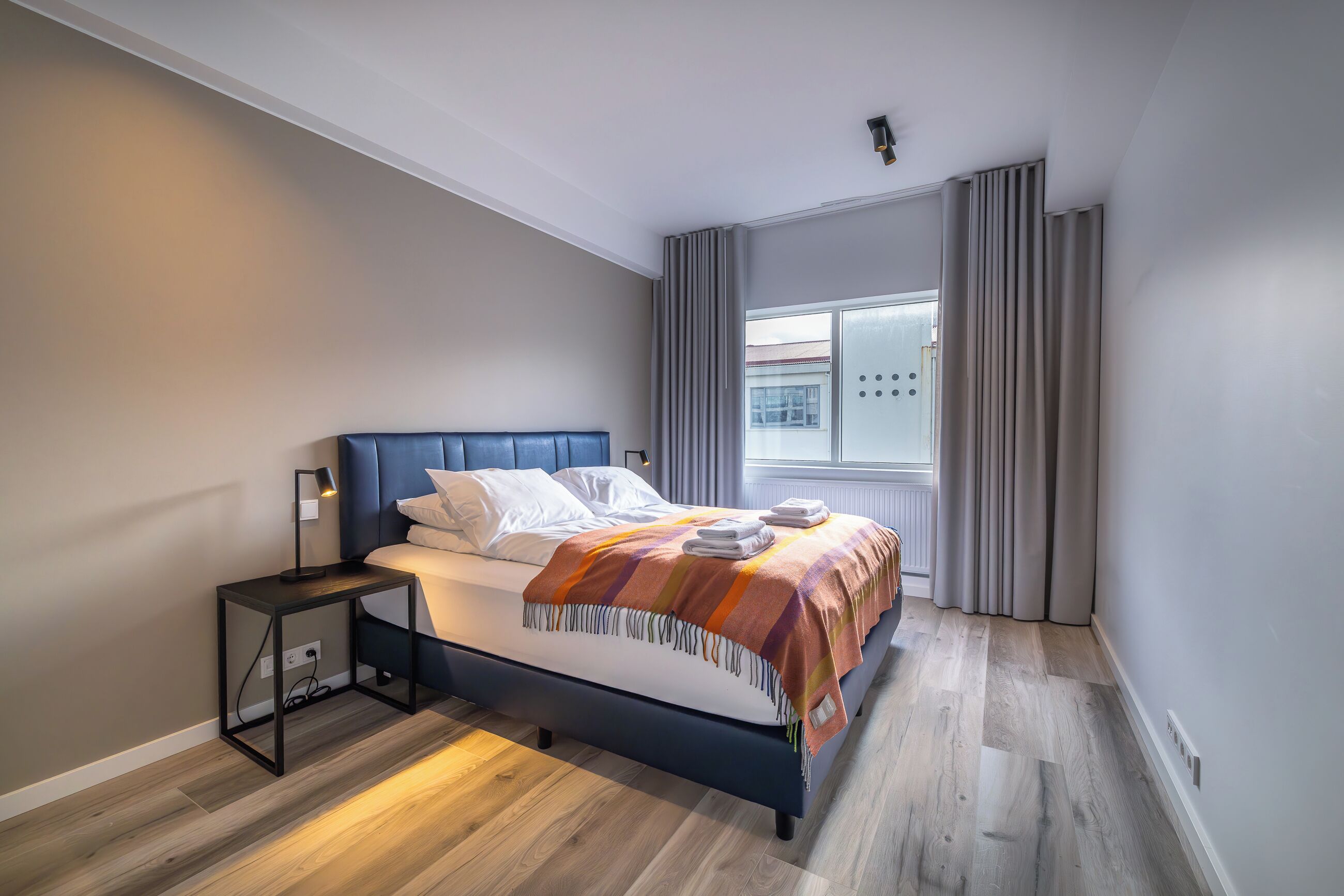 A modern bedroom with a bed, bedside table, and a window with curtains.