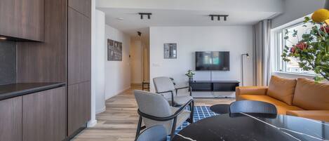 A modern living room with a black marble table, grey and black chairs, a brown sofa, and a flat-screen TV mounted on the wall.