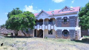 A two-story building with a red roof, a balcony, and a staircase leading to the upper floor. - Lux Suites Chief Engineer Apartments (Mwingi)