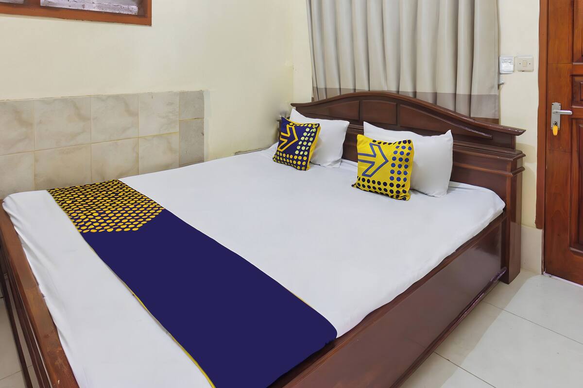 Una cama bien hecha con un edredón azul y amarillo, dos almohadas con un estampado azul y amarillo, y un cabecero de madera.