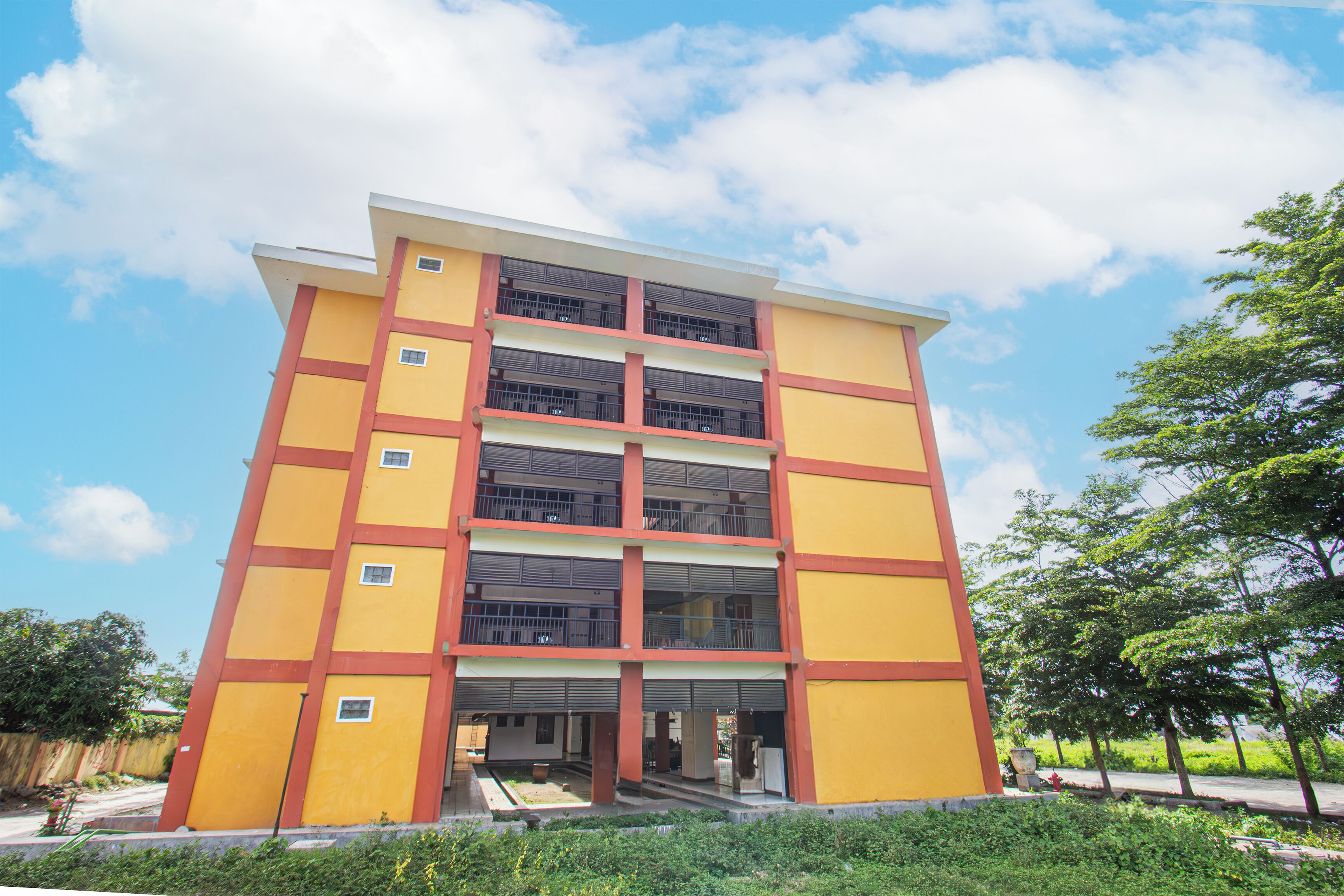 Un immeuble à plusieurs étages, doté d’une façade jaune et de touches de couleur rouge, avec des balcons et une entrée centrale.