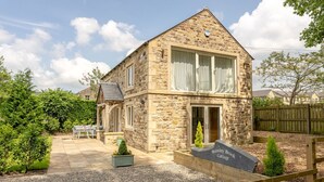 A stone cottage with a patio, outdoor seating, and a sign reading "Bramble Brook Cottage". - Bramley Brook Cottage 5 star Luxury (Whalley)