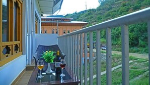 A balcony with a table set for two, featuring two wine glasses and a vase with flowers. - Punakha Residency Hotel (Punakha)
