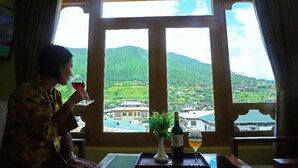 A person sitting by a window with a view of a green landscape and buildings. - Punakha Residency Hotel (Punakha)