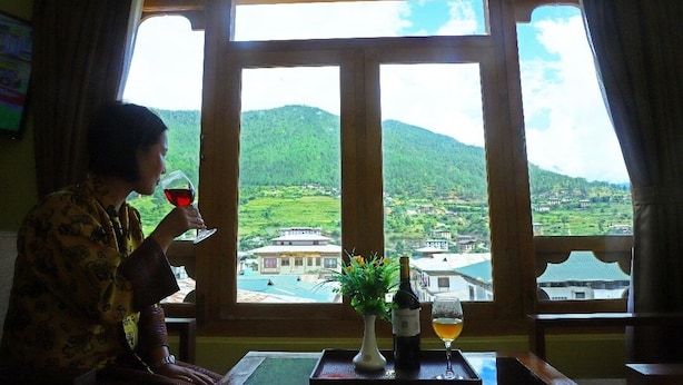 A person sitting by a window with a view of a green landscape and buildings. - Punakha Residency Hotel (Punakha)