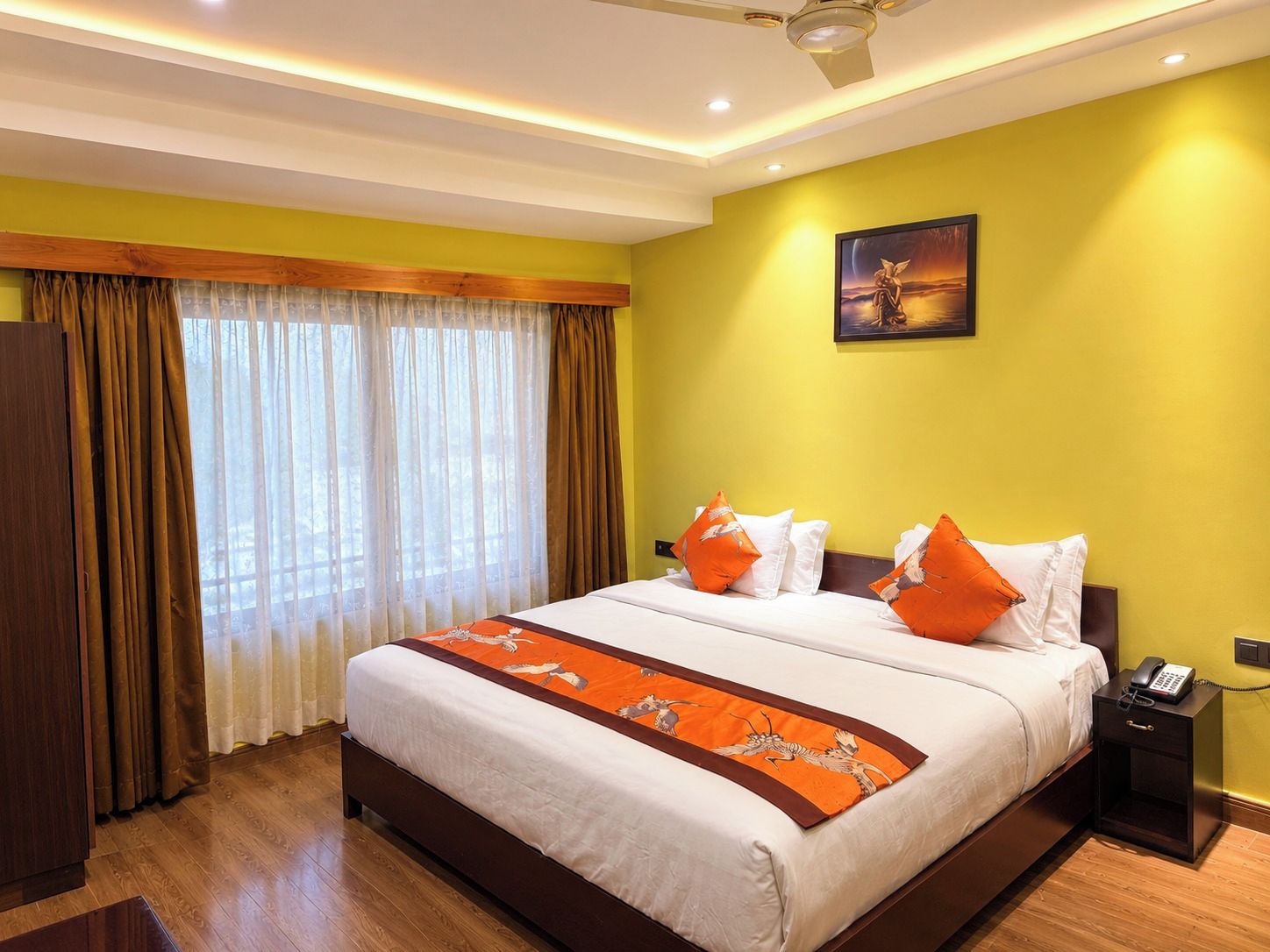 A hotel room with a large bed, a bedside telephone, and a painting on the wall.