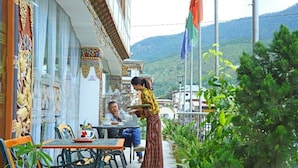 A terrace with a table and chairs, a person serving tea, and a mountain backdrop. - Punakha Residency Hotel (Punakha)