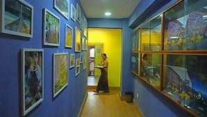 A hallway with framed pictures on the walls, a person walking, and a glass display case. - Punakha Residency Hotel (Punakha)