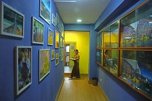 A hallway with framed pictures on the walls, a person walking, and a glass display case. - Punakha Residency Hotel (Punakha)