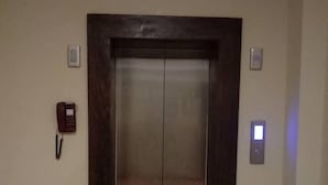 An elevator with a dark wooden frame, a red phone on the wall to the left, and a light switch to the right. - Punakha Residency Hotel (Punakha)
