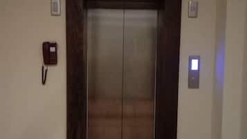 Un ascensor con estructura de madera oscura, un teléfono rojo en la pared a la izquierda y un interruptor de luz a la derecha.