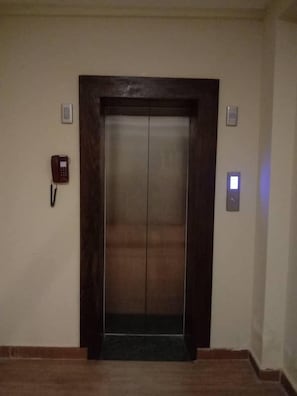 An elevator with a dark wooden frame, a red phone on the wall to the left, and a light switch to the right. - Punakha Residency Hotel (Punakha)