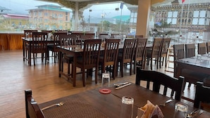 A restaurant with wooden tables and chairs, large windows with decorative ironwork, and a view of buildings outside. - Punakha Residency Hotel (Punakha)
