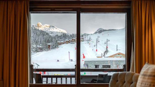 Ein Hotelzimmer mit großem Fenster mit Blick auf einen verschneiten Skipistenhang.
