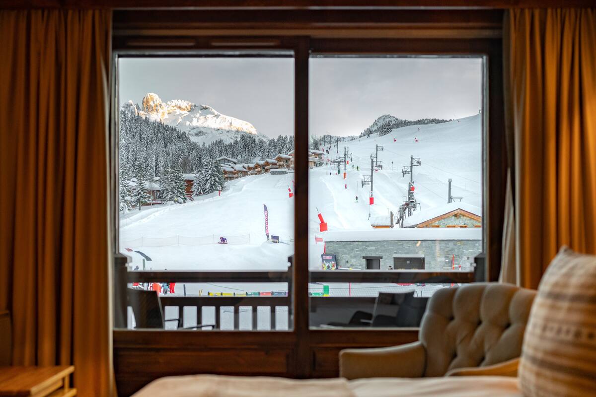 Quarto de hotel com uma grande janela com vista para uma encosta nevada para esquiar.