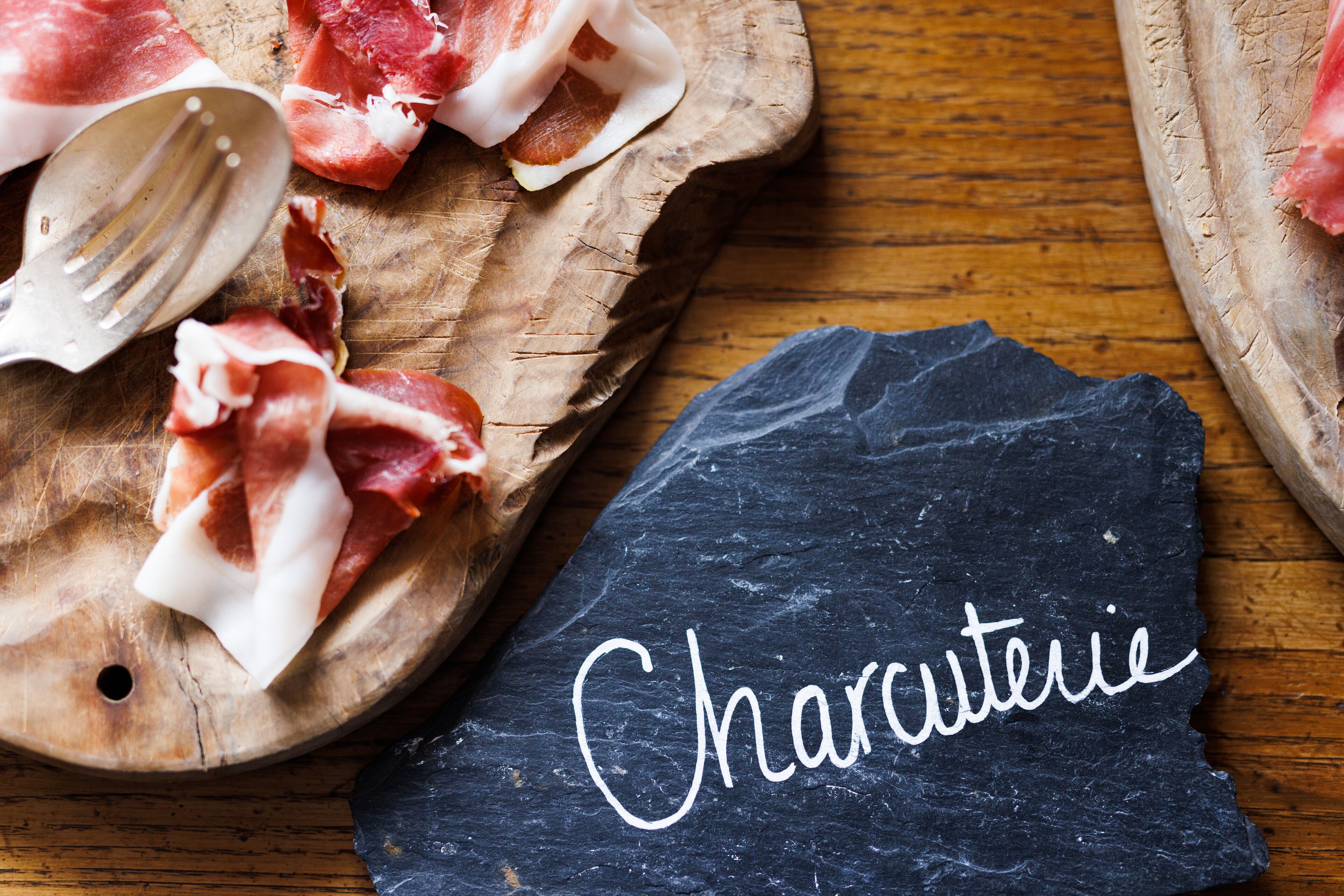 A wooden cutting board with sliced charcuterie and a slate with 'Charcuterie' written on it.