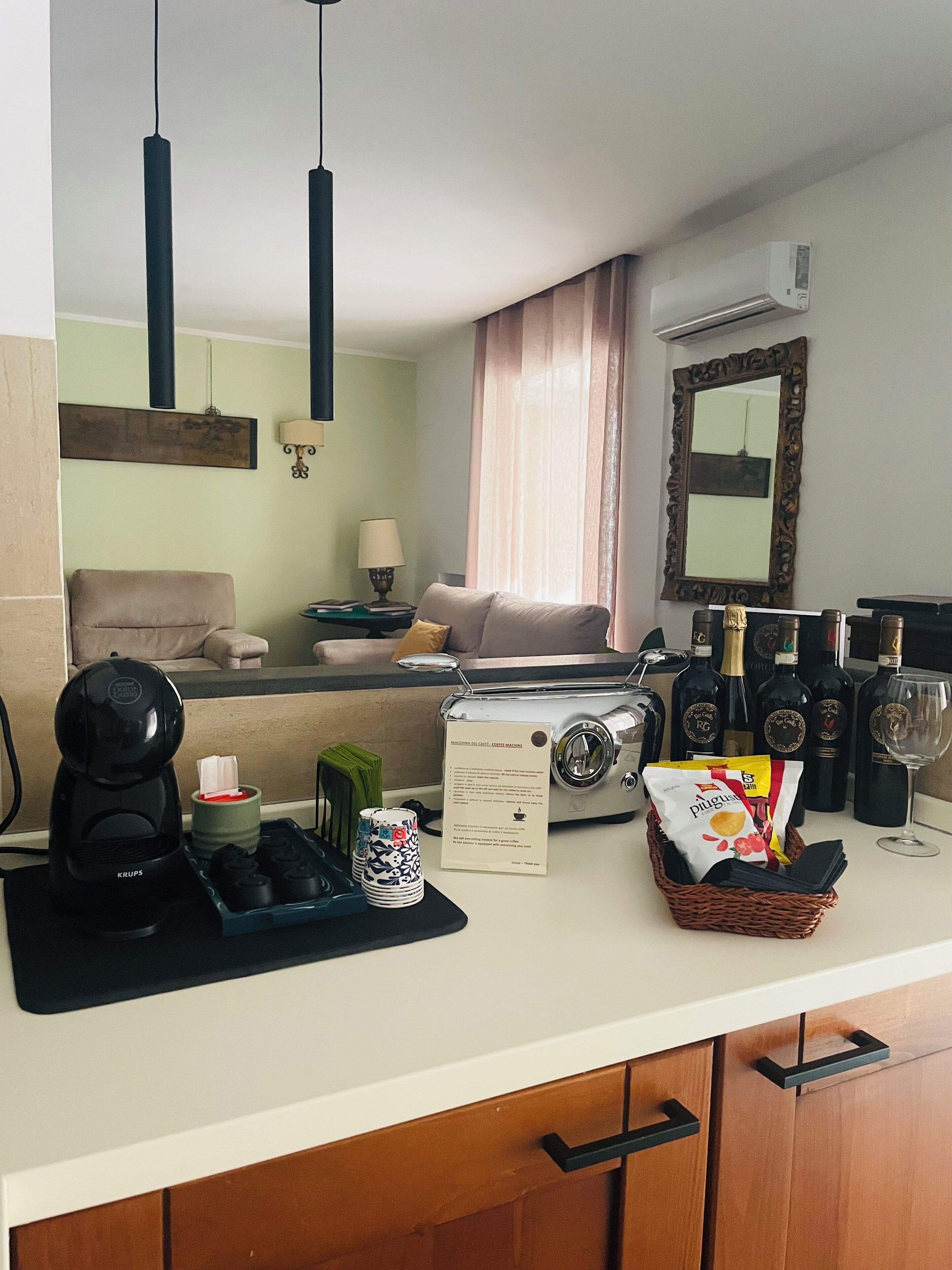 A compact kitchen with a coffee maker, tea set, and a basket of snacks.
