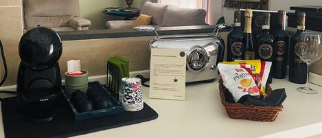 A compact kitchen with a coffee maker, tea set, and a basket of snacks.