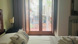 A hotel room with a bed, a nightstand, a lamp, a window with curtains, and a view of the outside. - Apartment Luxury Via Chiaia  (Napoli)