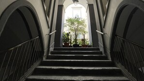 A staircase with a view of a building's interior, featuring arched doorways and a hanging light fixture. - Apartment Luxury Via Chiaia  (Napoli)