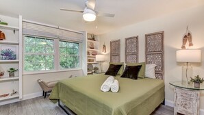 Un dormitorio ordenado con cama, una silla, una mesita de noche y una ventana con persianas.
