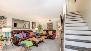 Una sala de estar con un sofá de cuero marrón, una mesa de centro de madera y una escalera con barandilla de madera.