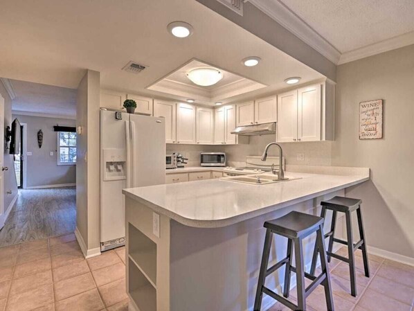 Una cocina moderna con armarios blancos, una isla grande con taburetes altos y luces empotradas en el techo.