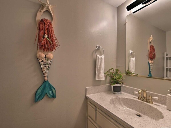 A bathroom with a sink, a mirror, a towel ring, and a decorative mermaid tail.