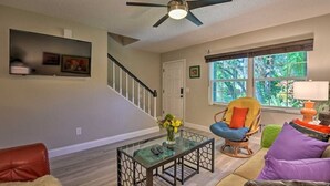 Un salon avec une table basse en verre, un fauteuil en osier, un canapé et un escalier.