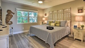 Une chambre à coucher comprenant un lit, un ventilateur de plafond, une fenêtre et une table de chevet avec une lampe.